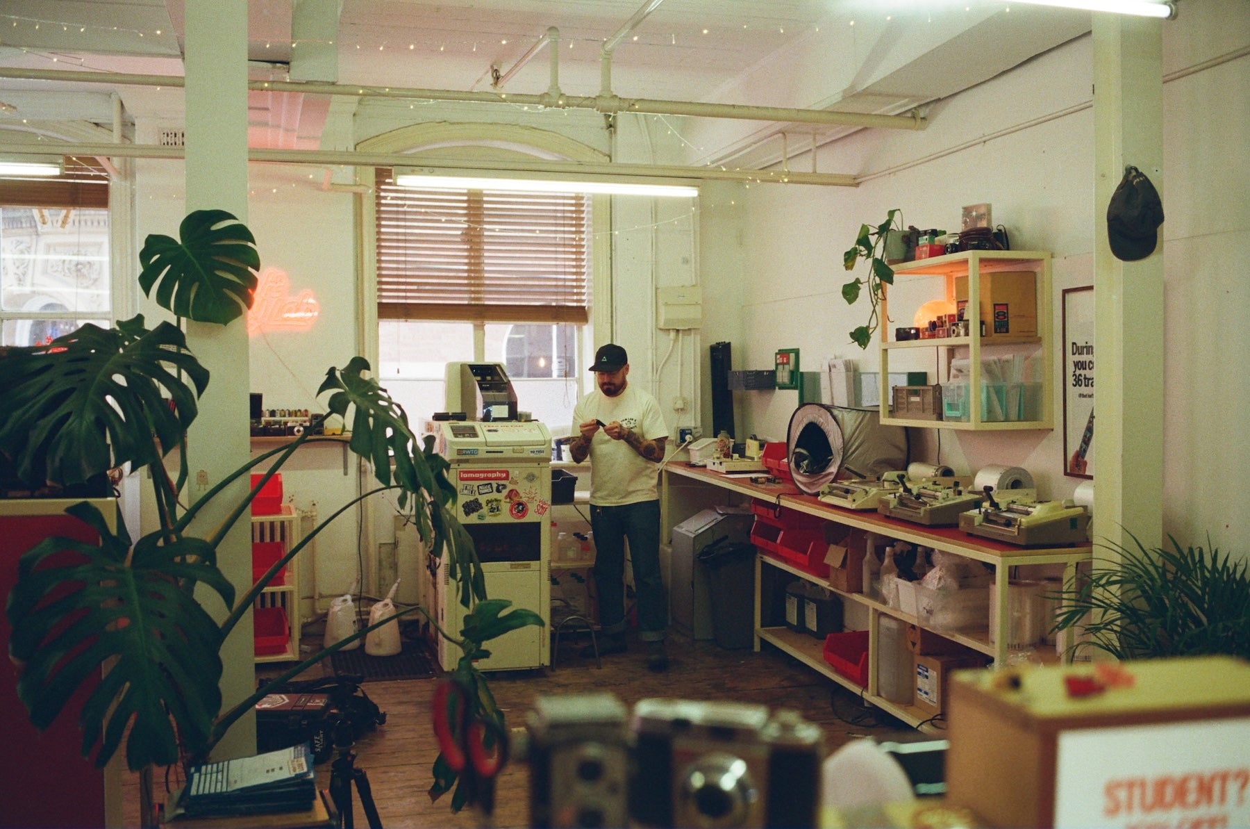 Person standing in a room with plants, shelves, and various items.