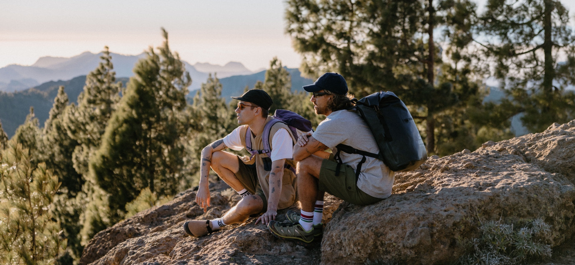 Two men sitting on a rock looking out over the view at sunset