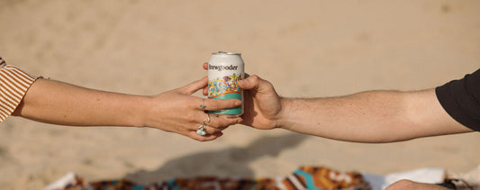 A man hands a woman a can of Brewgooder beer on the beach